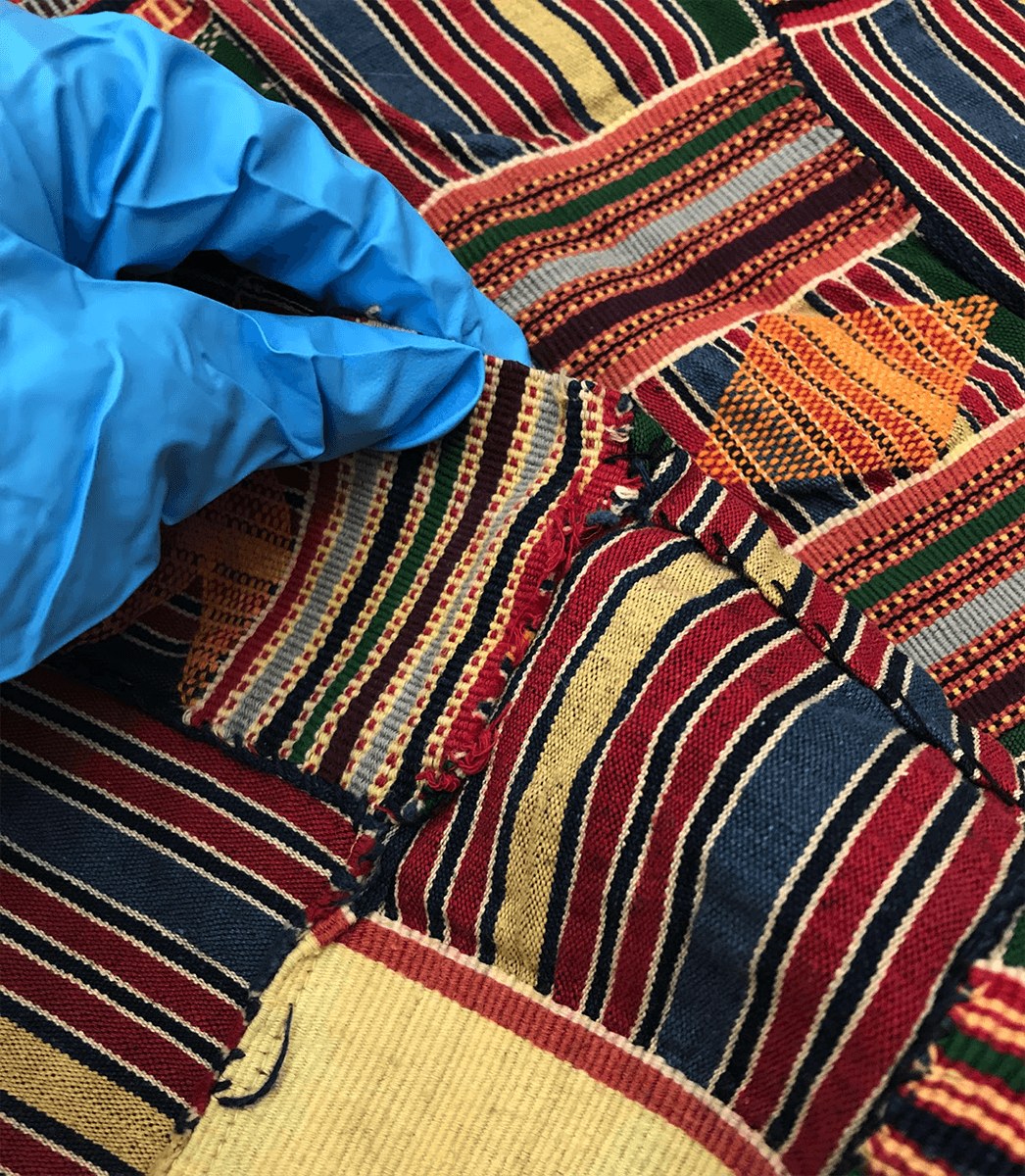 gloved hand examining patterned African textile