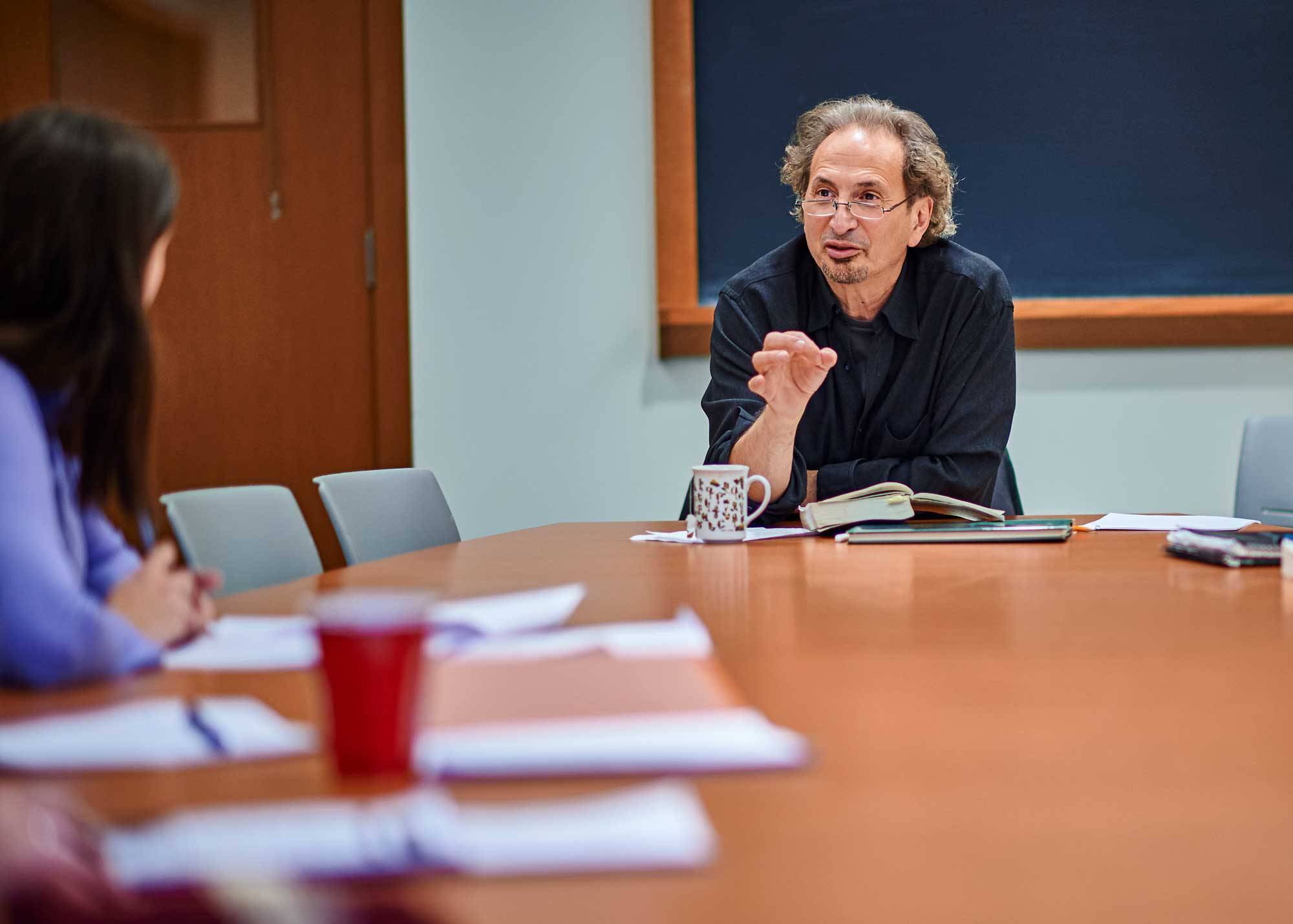 Professor Peter Balakian speaks to student while seated at a table