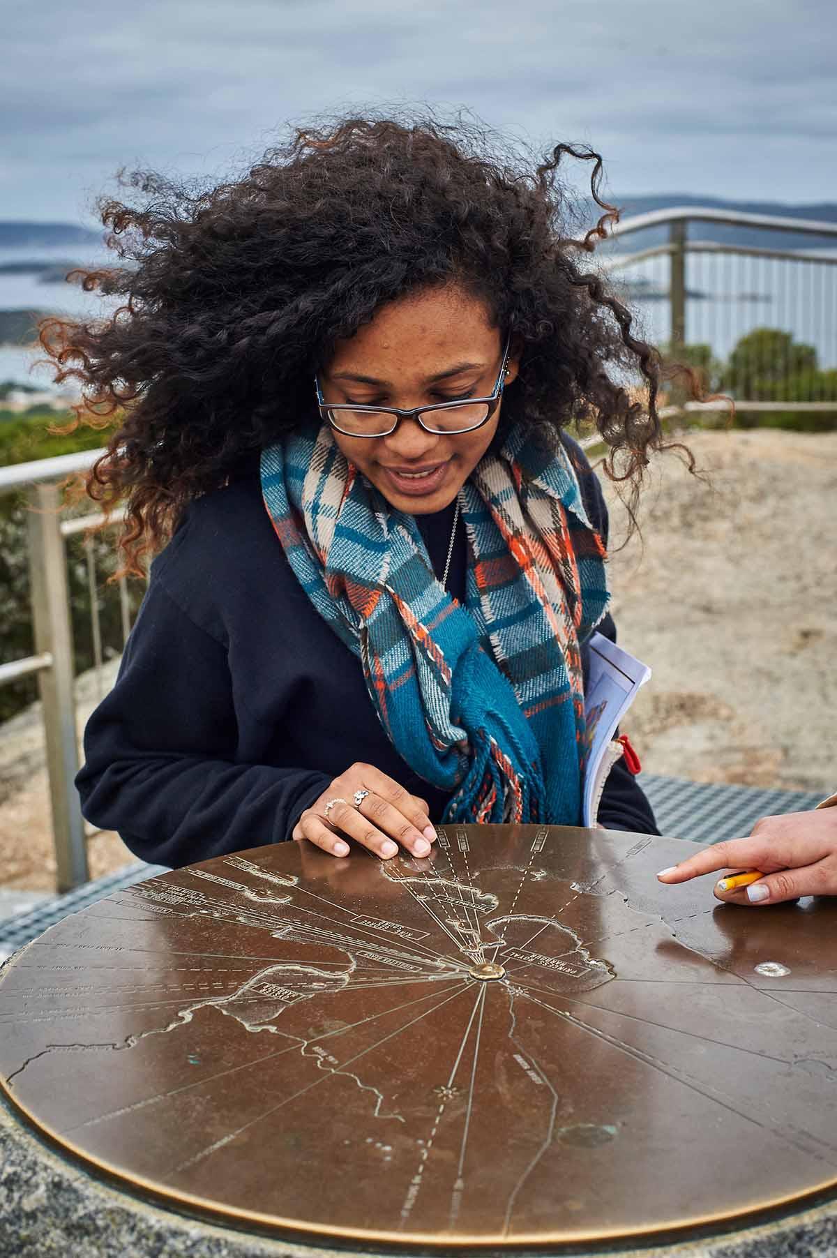 Student examines a brass map marker at a scenic overlook in Australia The Department of Geography co-sponsors, with the Environmental Studies Program, a semester-long study group at the University of Wollongong (UoW) in Australia during both the  fall and spring semesters.