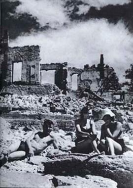 People appearing to lounge, as if at a beach, but amidst the ruins of a war