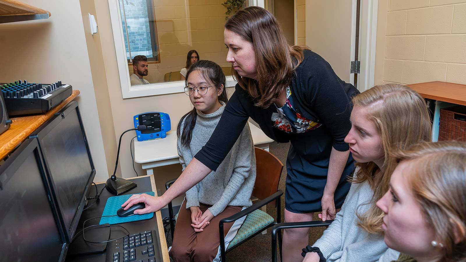 Jen Tomlinson and students work at a computer while research subjects are monitored in the background