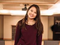 A women smiles and looked at the camera and is wearing a burgundy dress.