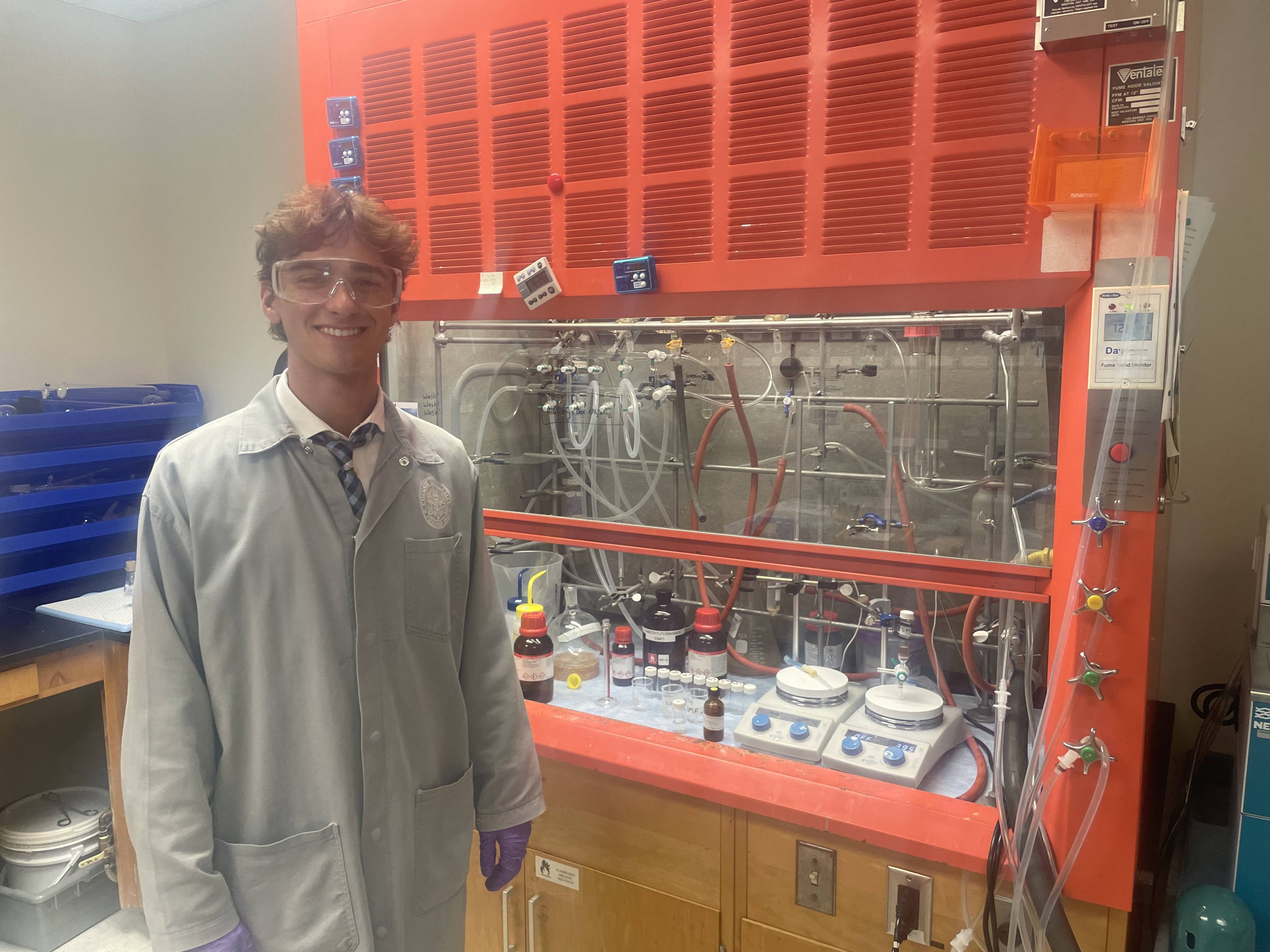 Scholar Liam McCarthy poses in front of a hood full of chemicals