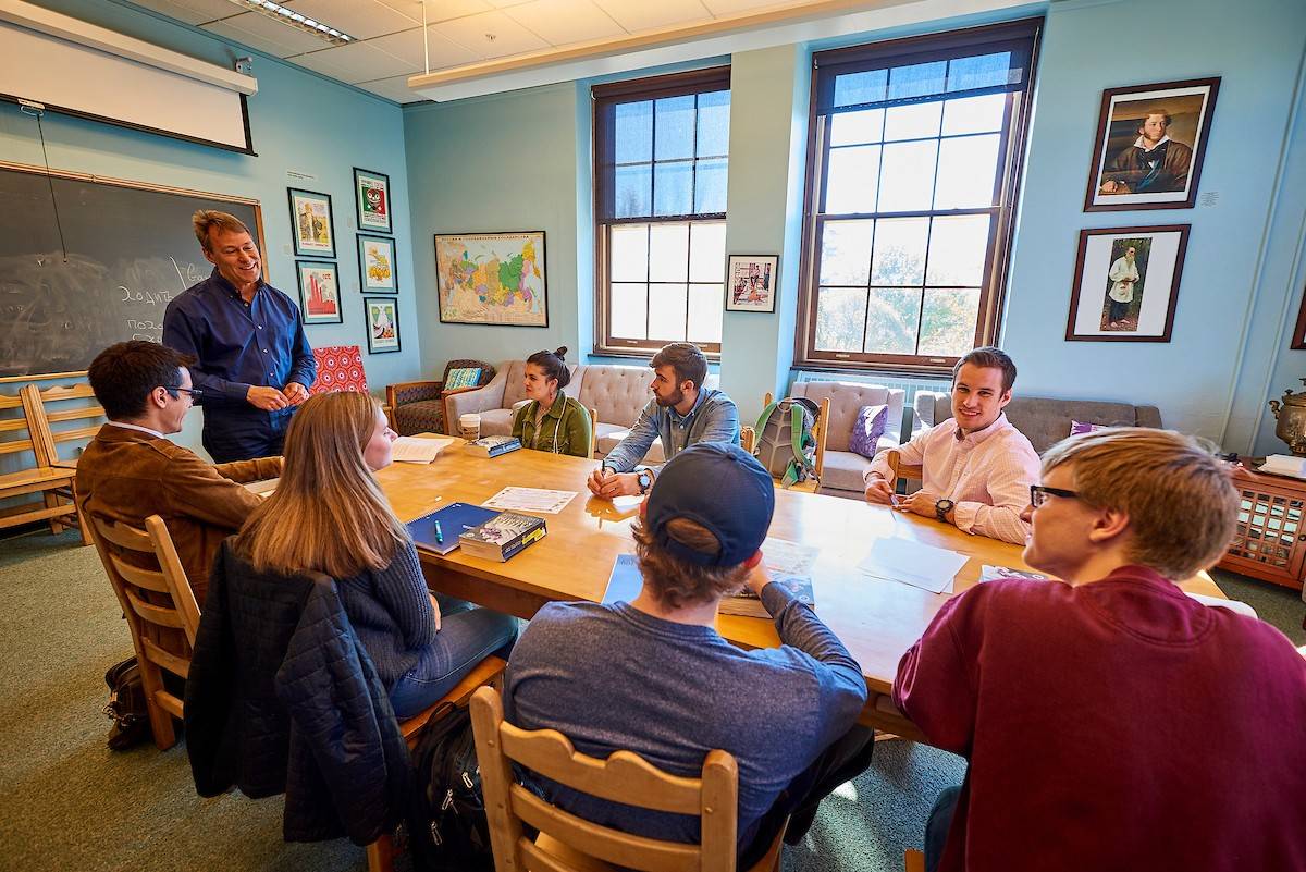 A professor and his class discuss coursework around a table