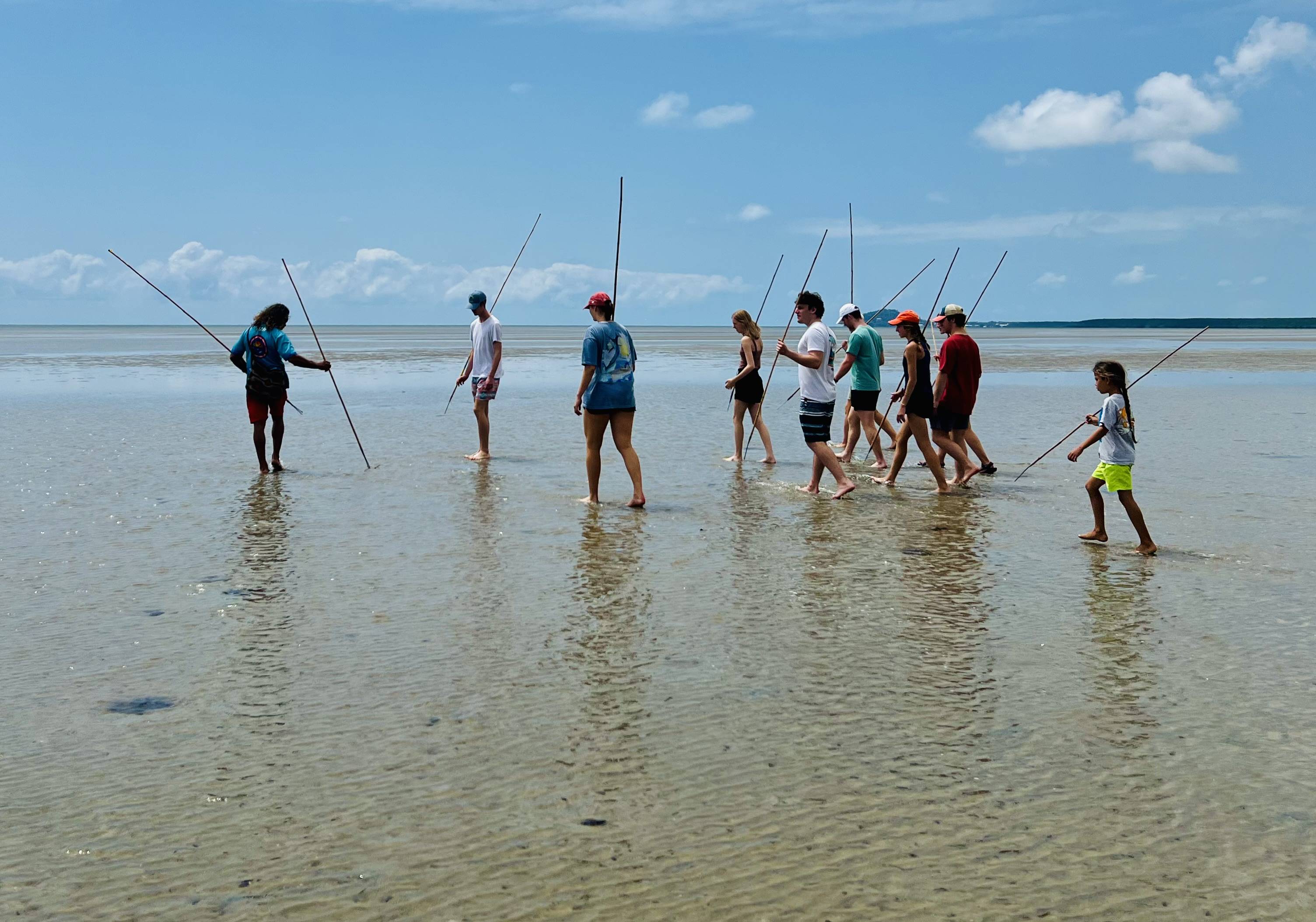 Photo of students standing on the beach carrying spears.