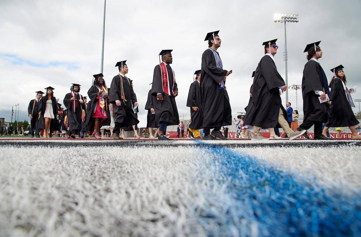 A line of graduates walk across the field during Commencement