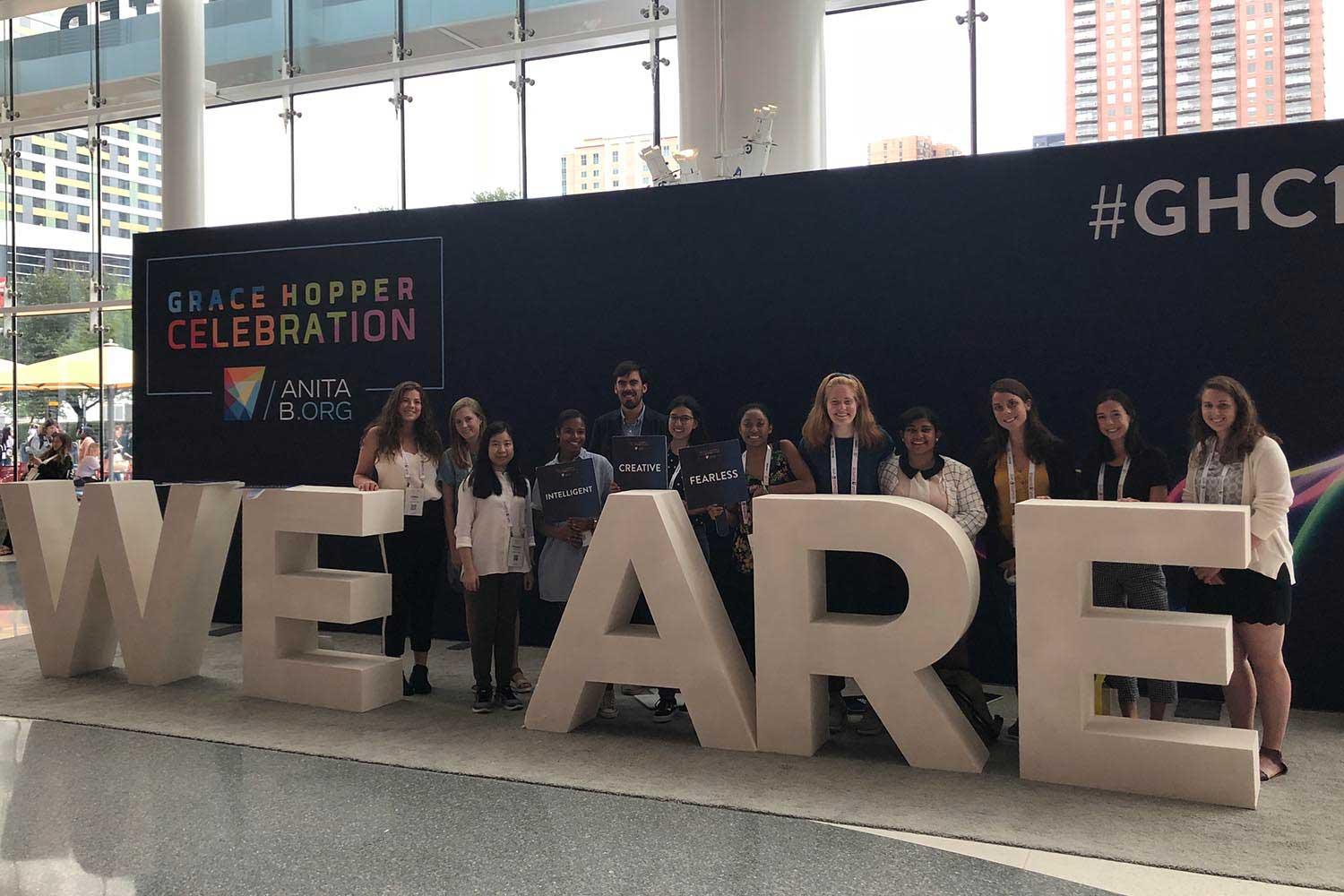 Colgate computer science students stand behind large letters spelling WE ARE