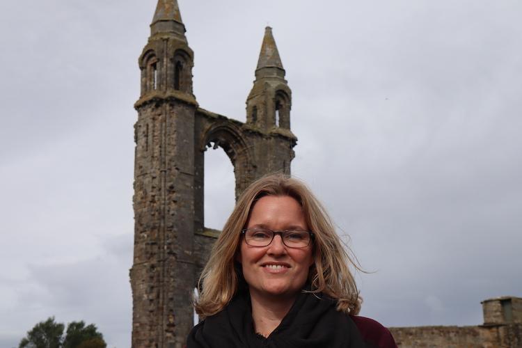 Smiling woman stands in front of religious structure on cloudy day